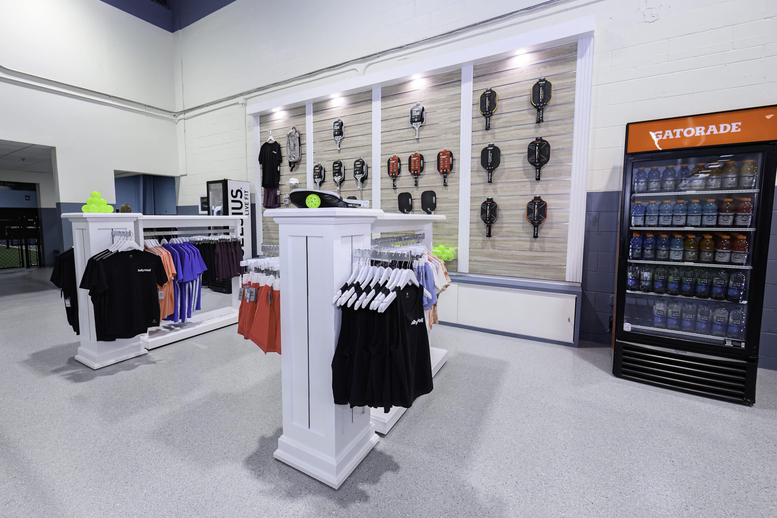 RallyWell pro shop with pickleball paddles, apparel, and a Gatorade cooler on display