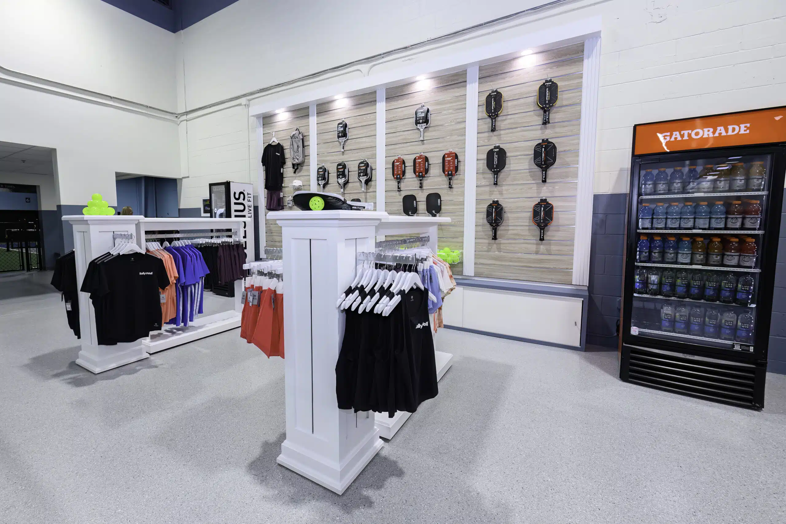 RallyWell pro shop with pickleball paddles, apparel, and a Gatorade cooler on display