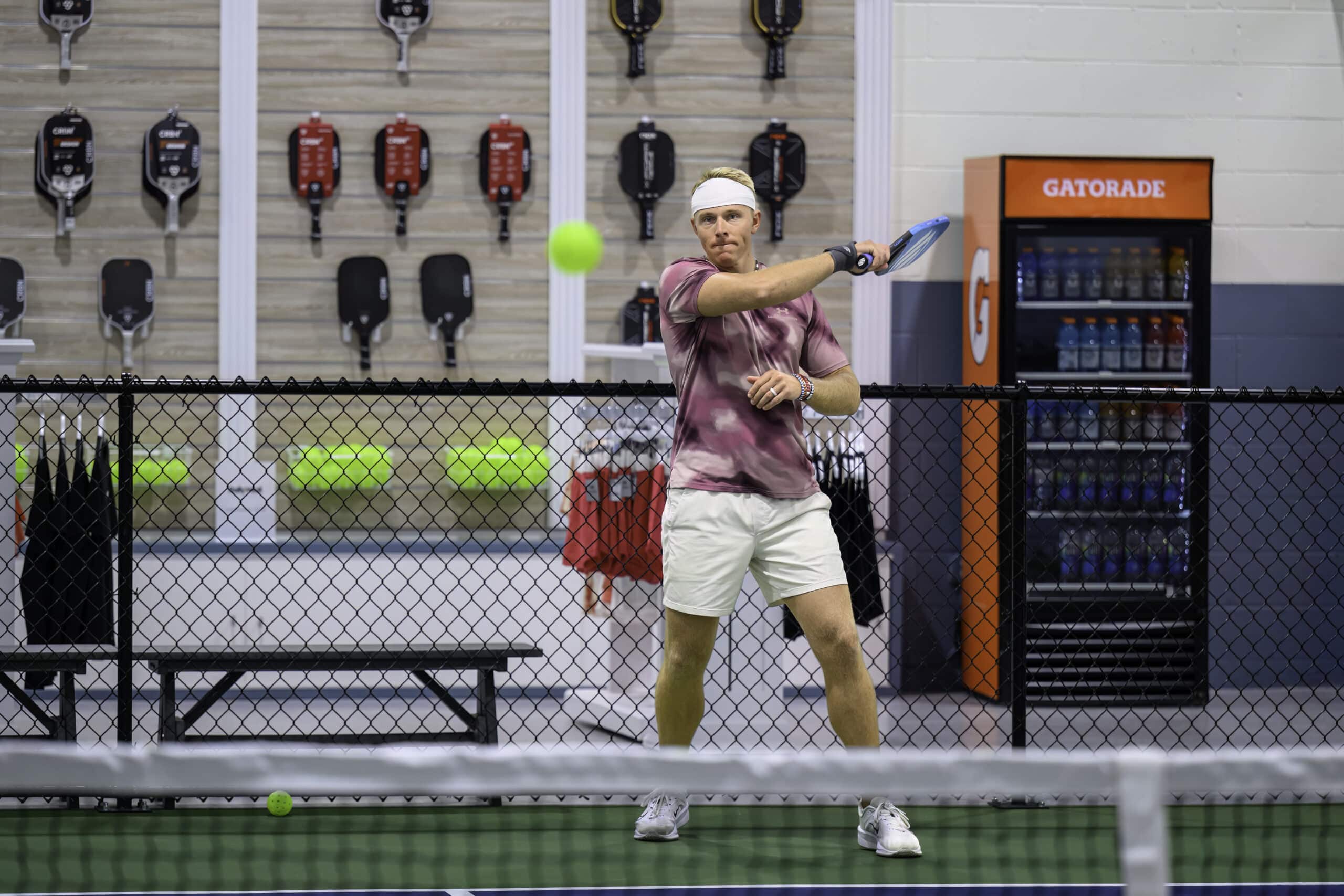 RallyWell player in a pink shirt lining up a backhand shot in the pro shop area