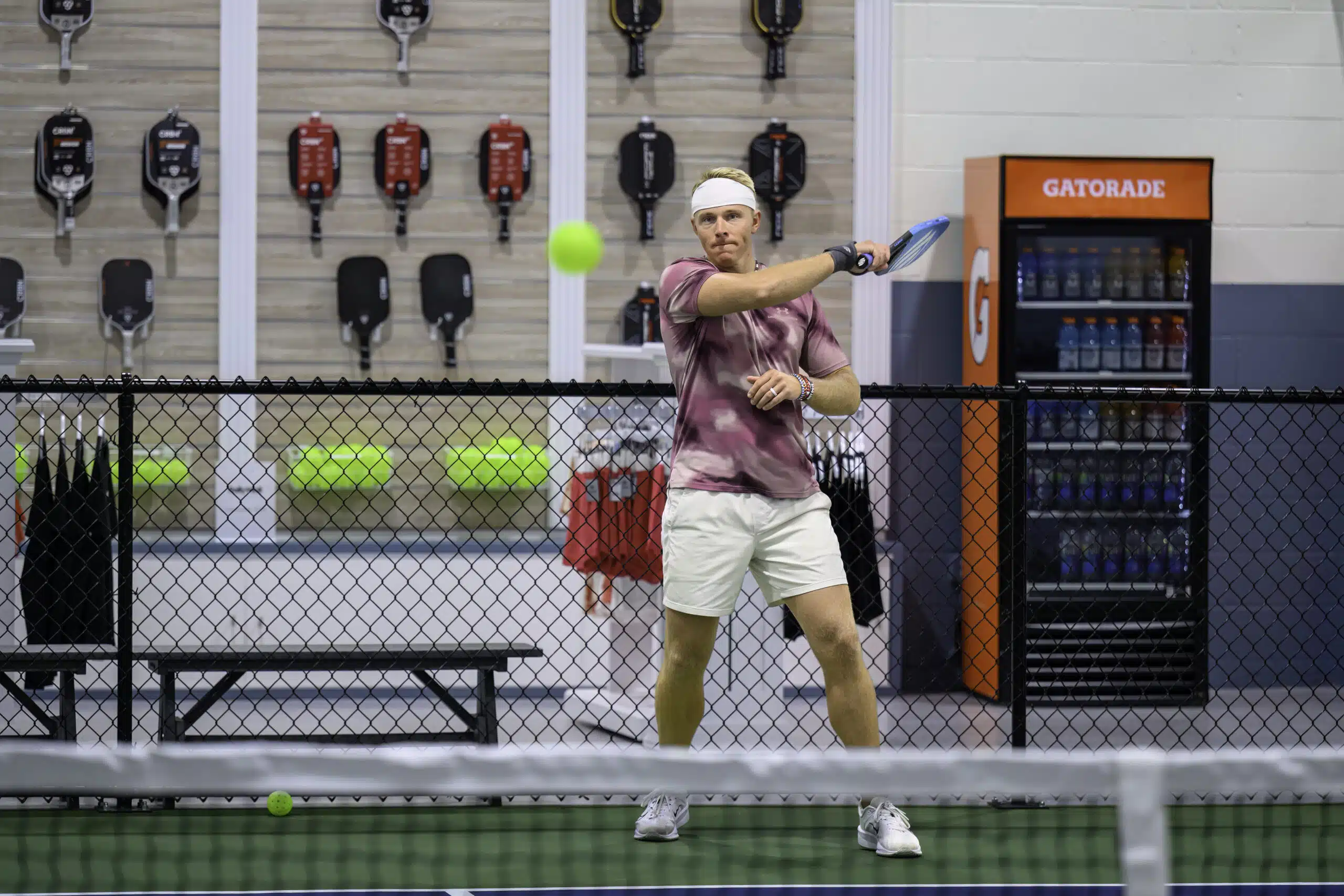 RallyWell player in a pink shirt lining up a backhand shot in the pro shop area