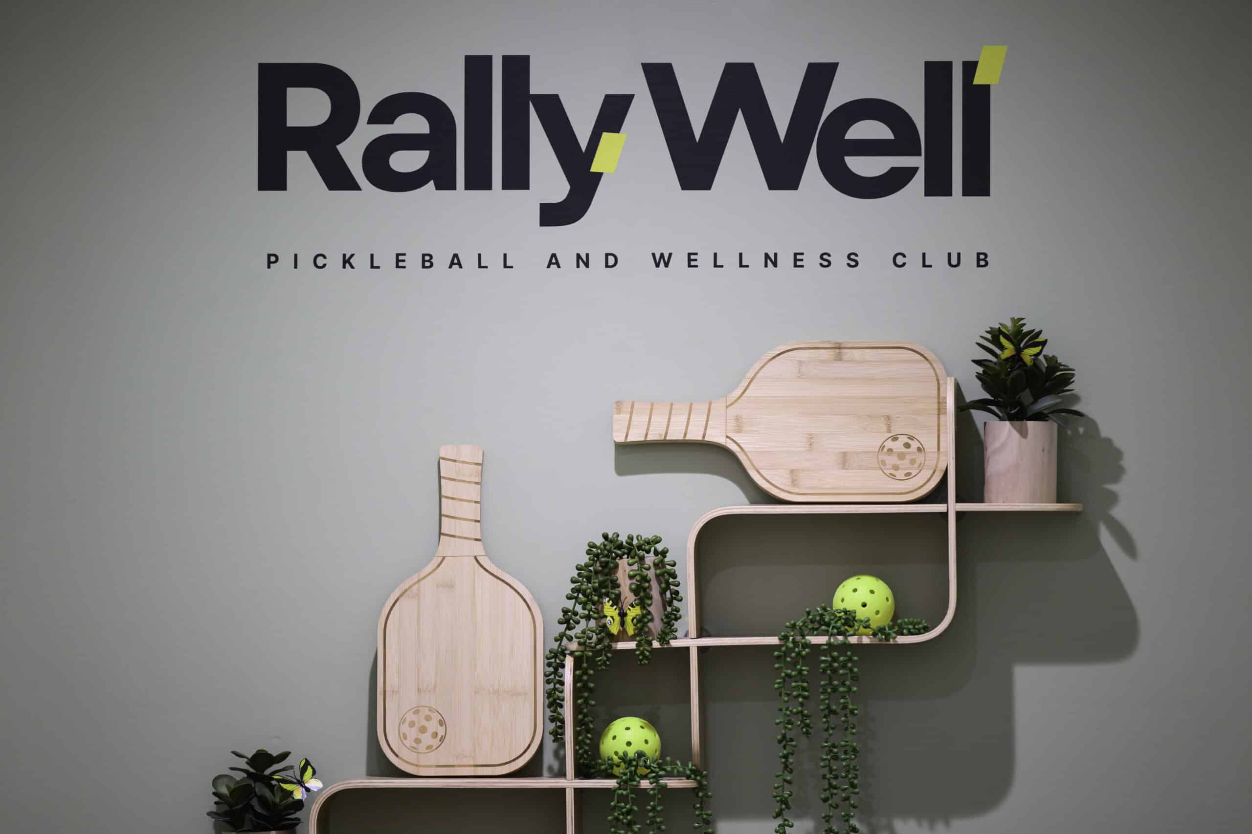 RallyWell logo wall display with a wood paddle accent and potted plants in the lobby