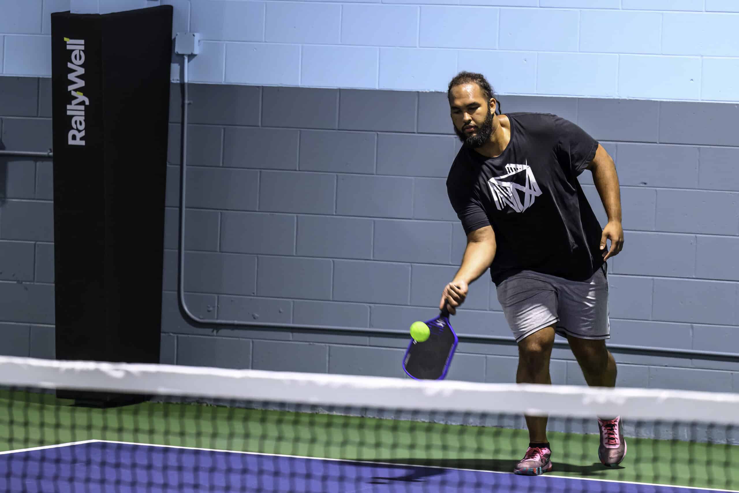 Player at RallyWell indoor pickleball club reaches to return a serve at the net