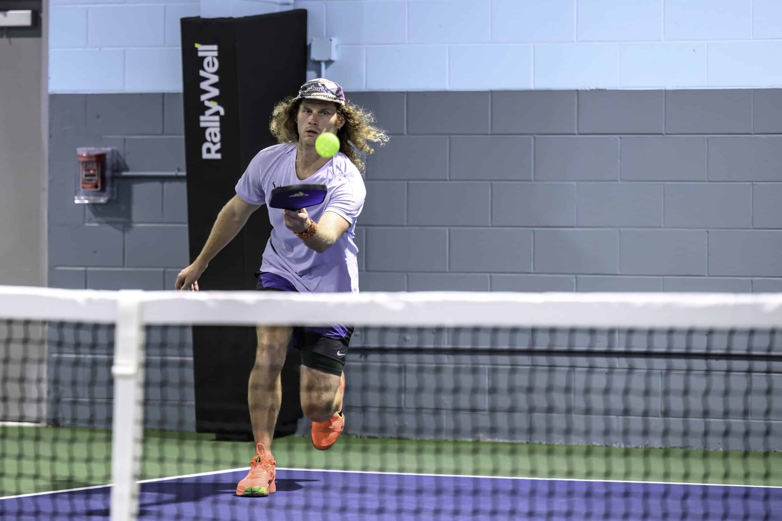 RallyWell player mid-swing hitting a shot on the indoor pickleball court