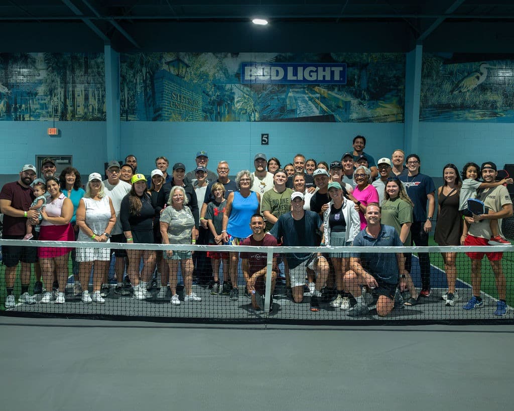Large group of RallyWell members posing together on the indoor pickleball courts