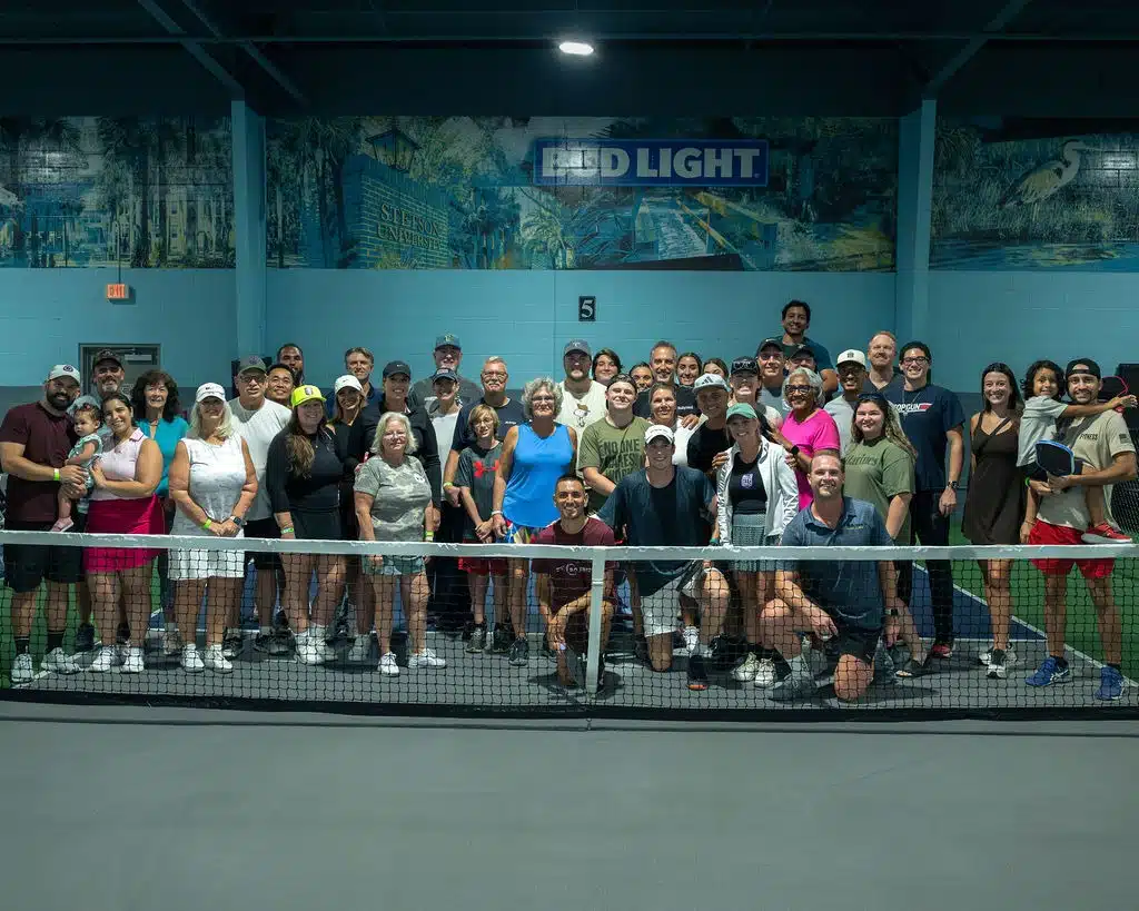 Large group of RallyWell members posing together on the indoor pickleball courts